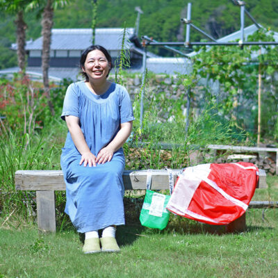 のどかな緑の芝生が広がる庭で、HOZUBAGを持ってベンチに座る工場長の武田さん。