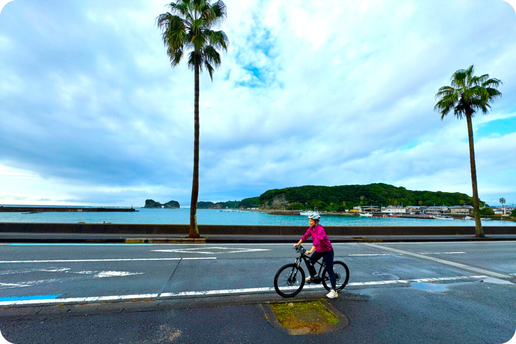 透き通るようなブルーの海と空を背景に、自転車にまたがる日髙さん